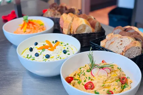 Drei Schüsseln mit Aufstrichen und Dips, dahinter Körbe mit hellem und dunklem Brot