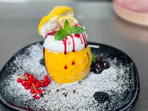 Gefüllte Zitrone mit Sahnehaube, Beerensauce und Minze auf schwarzem Teller