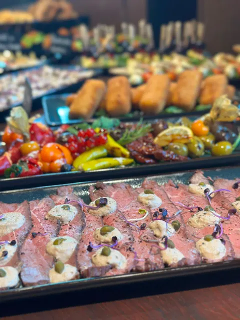 Rosa gebratenes Roastbeef mit Kapernrahm, Kapern und Kresse, dahinter Antipasti und Kroketten