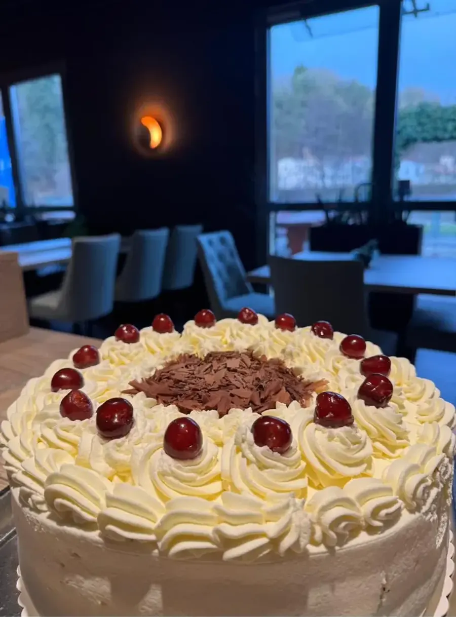 Sahnetorte mit Kirschen, dahinter der Gastraum